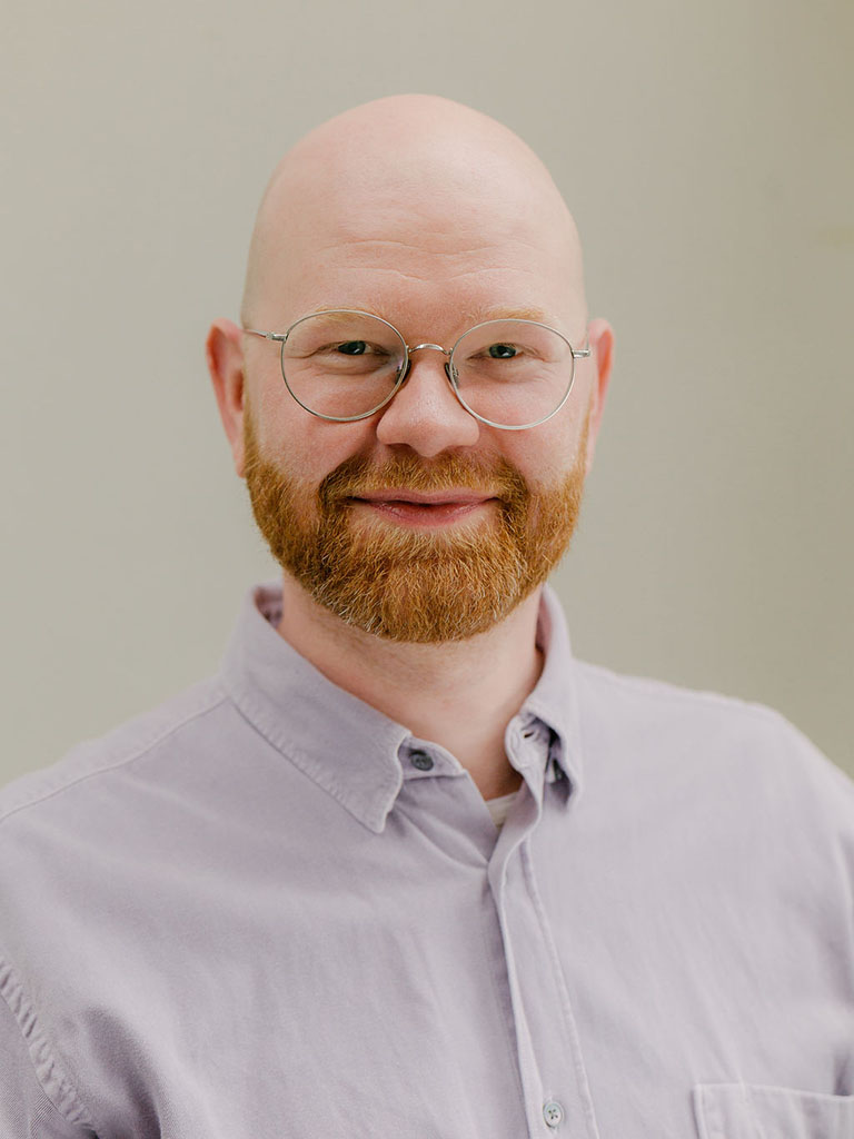 Ein Portrait von einem Mann mit Bart und Brille der lächelt