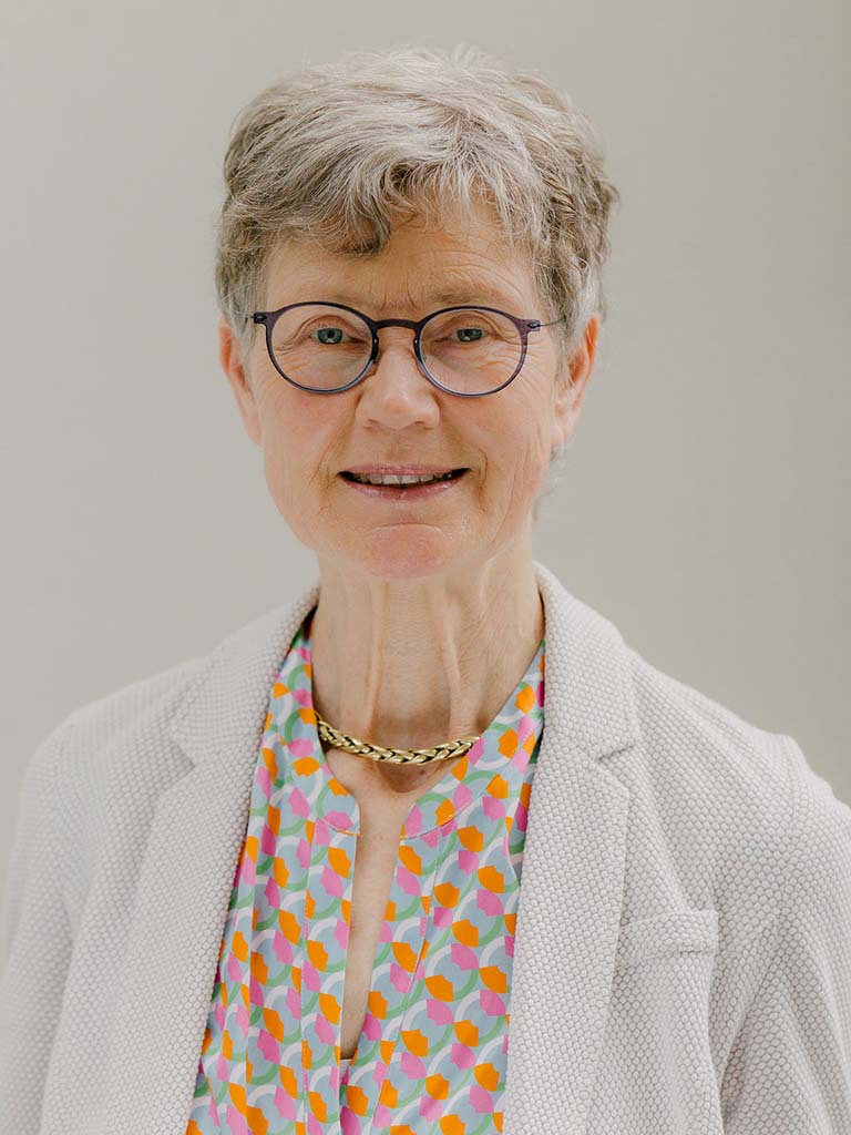 Ein Portrait von einer älteren Frau mit kurzen grauen Haaren und Brille die lächelt