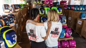 Zwei Frauen mit dem Rücken zur Kamera die sich in den armen haben und vor Schultaschen stehen