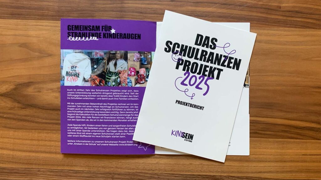 Bild von zwei Broschüren, eines ist aufgeklappt drauf liegt eine zweite in geschlossener Form mit dem Titel: Das Schulranzenprojekt 2025 Projektbericht Kindsein Stiftung.