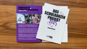 Bild von zwei Broschüren, eines ist aufgeklappt drauf liegt eine zweite in geschlossener Form mit dem Titel: Das Schulranzenprojekt 2025 Projektbericht Kindsein Stiftung.