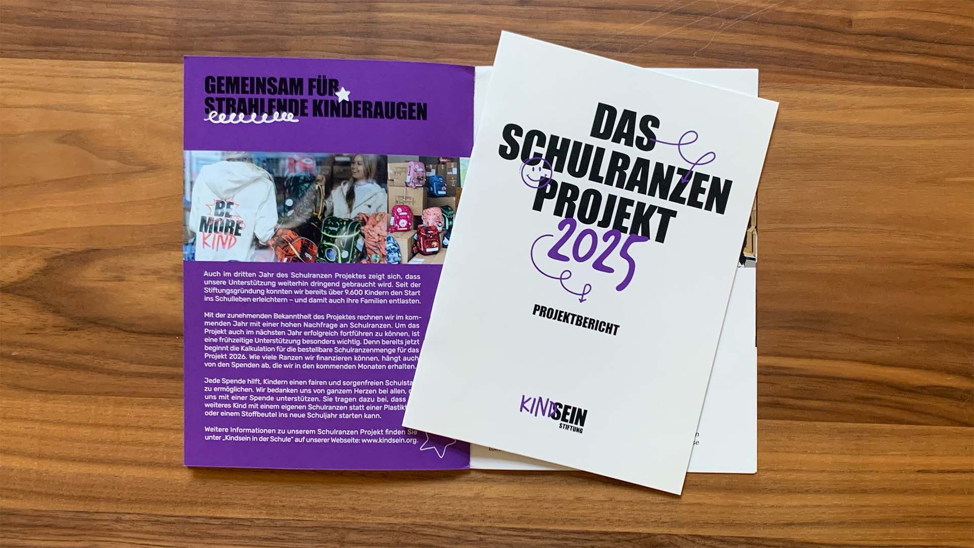 Bild von zwei Broschüren, eines ist aufgeklappt drauf liegt eine zweite in geschlossener Form mit dem Titel: Das Schulranzenprojekt 2025 Projektbericht Kindsein Stiftung.