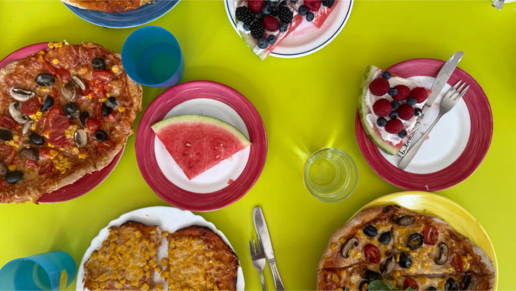 Tisch mit grüner Tischdecke und Tellern mit Wassermelone, Pizza, Beeren